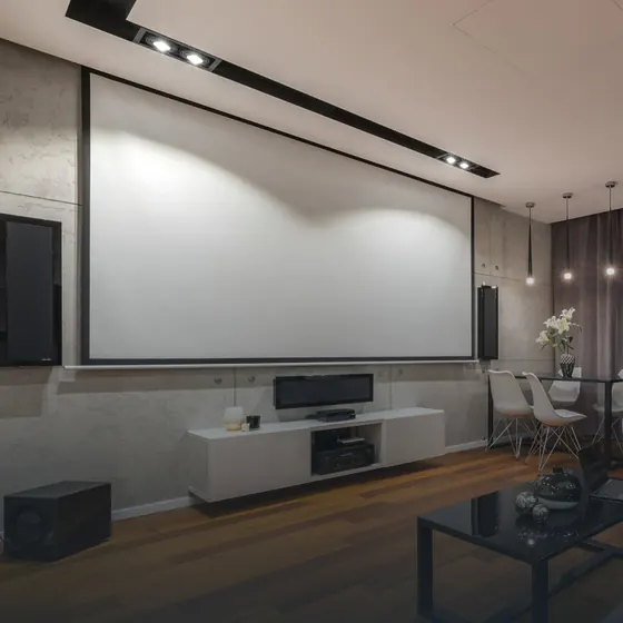 Sala de cinema com tela de projeção, caixas de som embutidas e spots no teto.