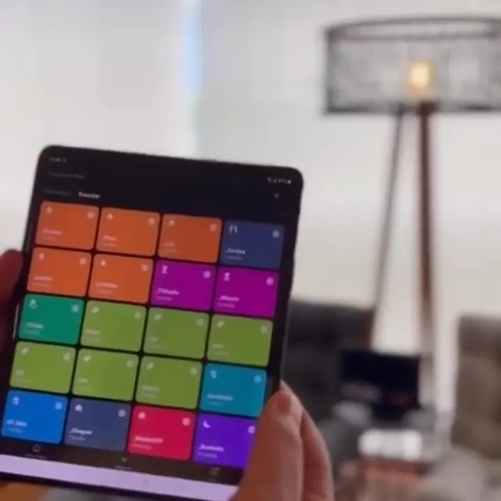 Celular dobrável aberto com o app de cenas em botões coloridos, numa sala com luminária de pé.