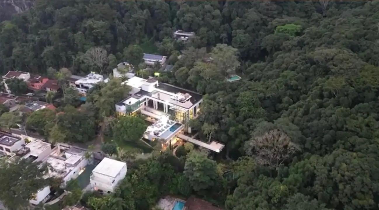 Vista aérea de dia de uma casa com piscina cercada pela mata.
