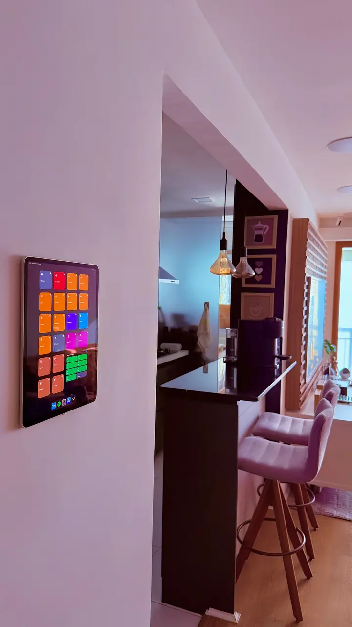 Tablet de controle na parede ao lado da bancada da cozinha, com a casa em luz rosada de fim de tarde.