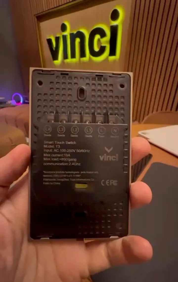 Verso de um interruptor touch Vinci, com as saídas identificadas, diante do letreiro vinci iluminado.