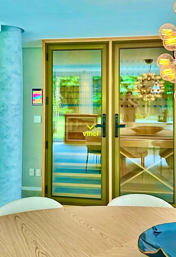 Sala de jantar com portas de vidro, tablet de controle na parede e pendente de lâmpadas de filamento.