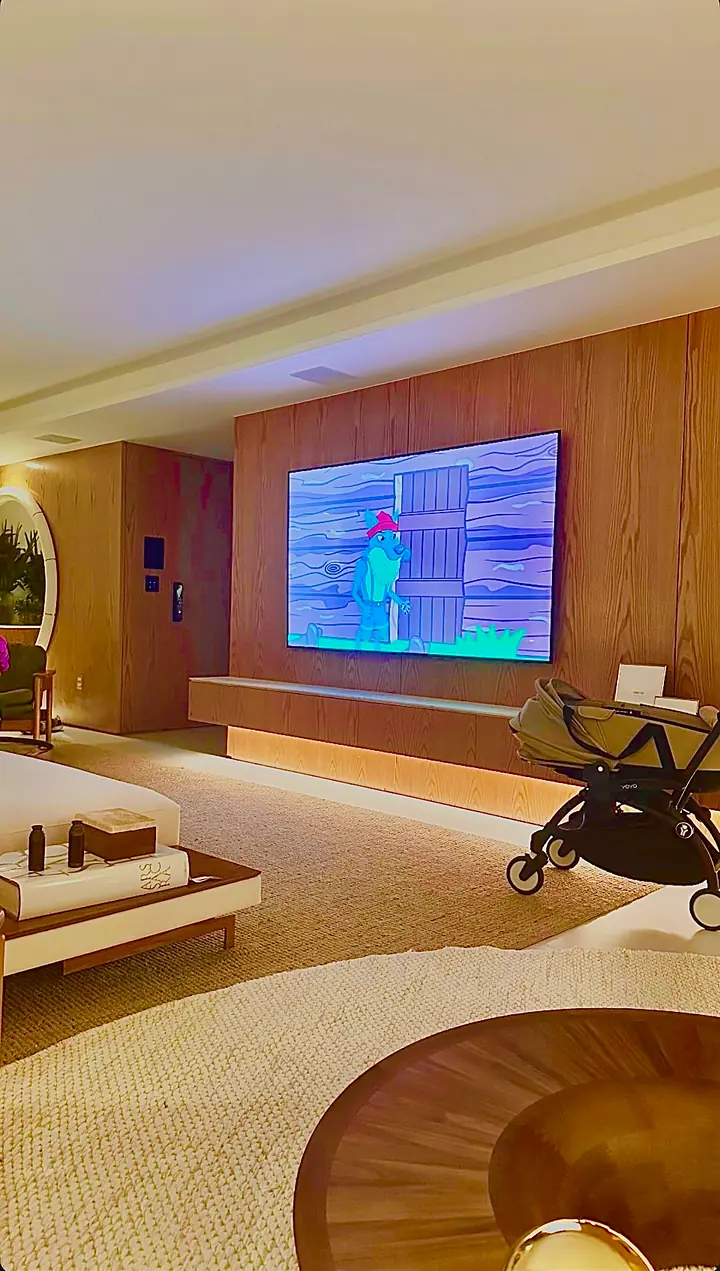 Sala de TV com painel de madeira, TV grande, rack suspenso com LED embaixo e teclados e fechadura digital na parede.