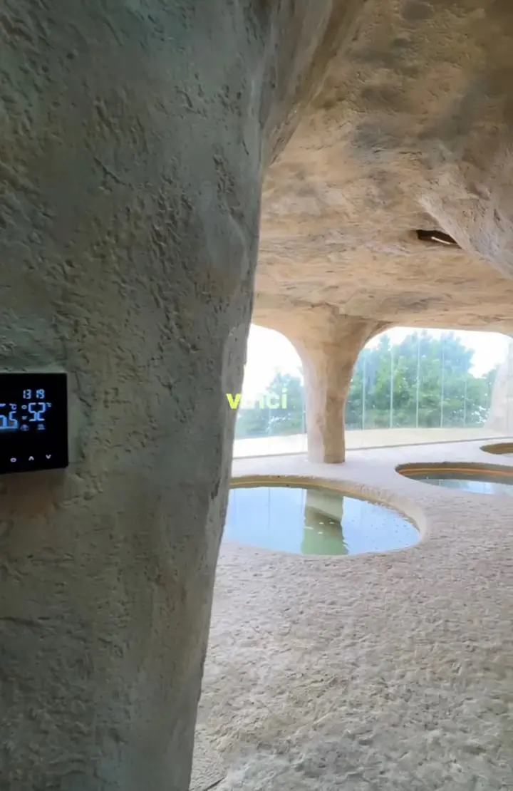 Spa em forma de gruta, com piscinas redondas, e um termostato digital na parede de pedra.
