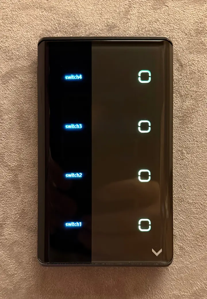 Interruptor touch de vidro preto com quatro teclas e legendas iluminadas, em parede de textura bege.