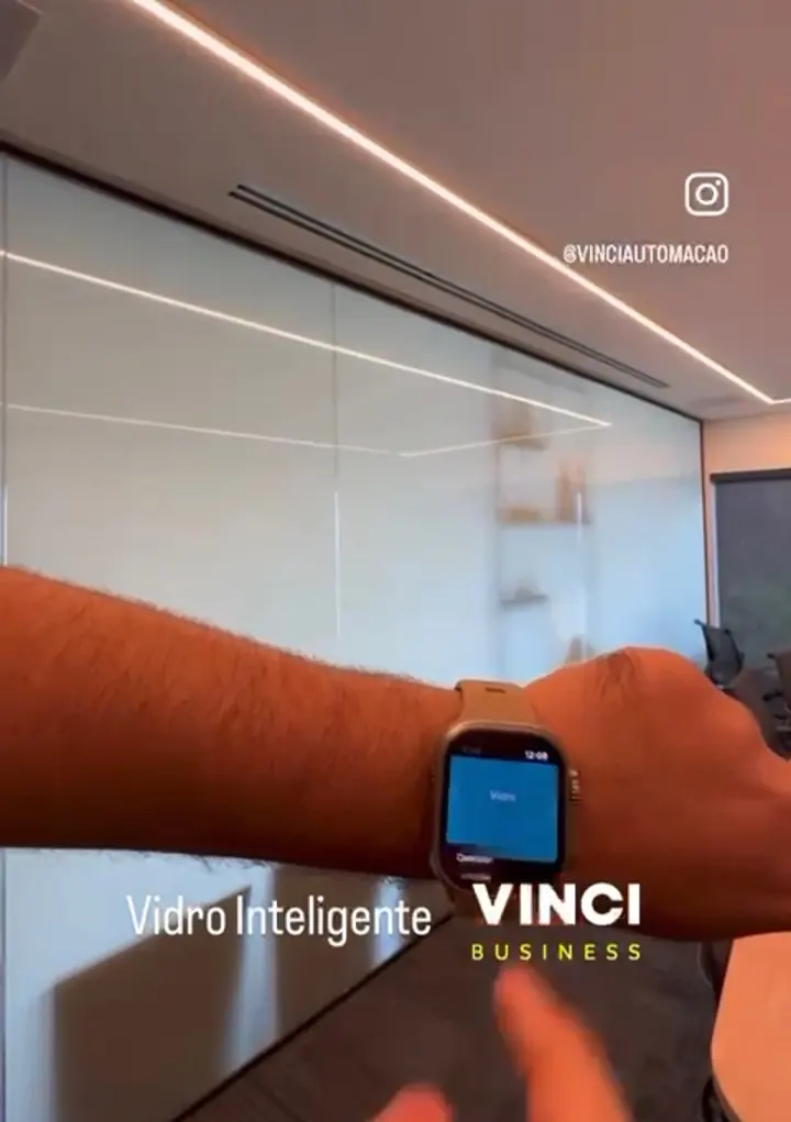 Pessoa aciona pelo relógio o vidro inteligente de uma sala de reunião, que fica fosco. Na imagem, a marca Vinci Business.