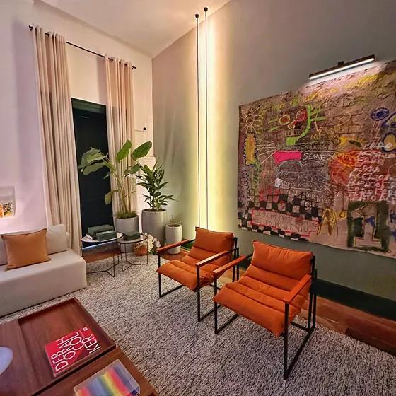 Sala com poltronas laranja iluminada por perfis de LED verticais do teto ao chão.